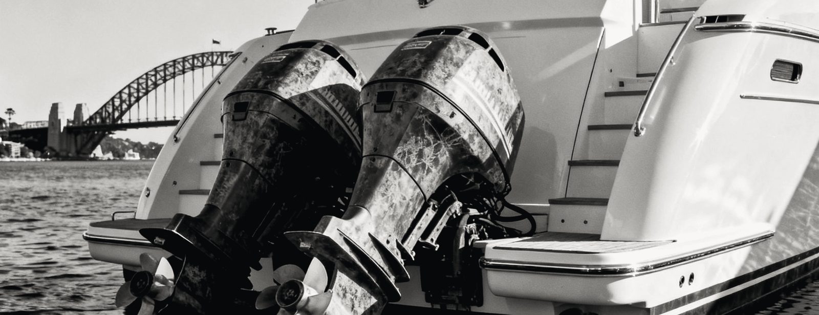 Detail of twin outboard engines and a white hull at rest on flat water