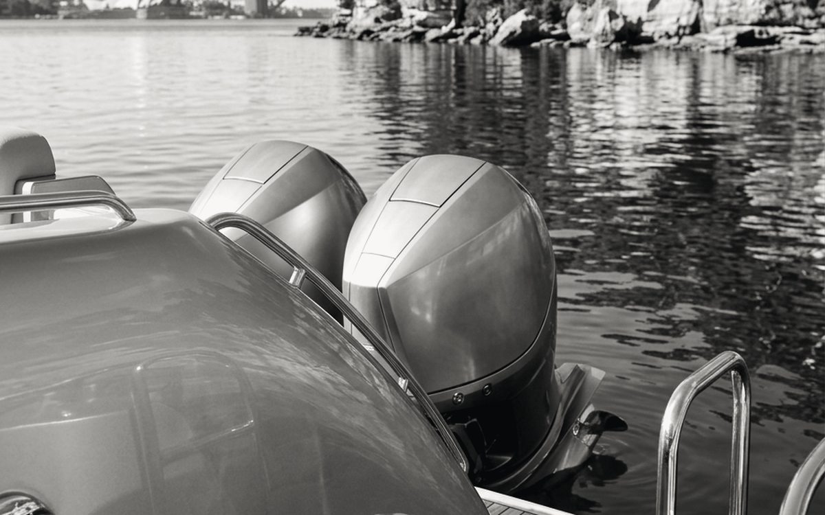 Twin outboard engines on the stern of a motor boat, sandstone shoreline behind